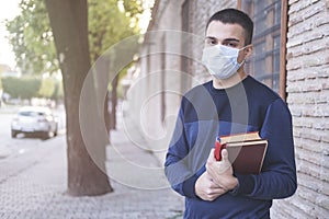 Portrait of confident male student holding books while standing in university campus with pandemics mask