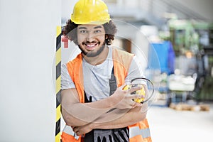 Portrait of confident male worker in protective clothing holding ear protectors at factory