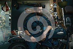 Portrait of confident man in overalls holding wrench while sitting on motorcycle