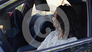 Portrait of confident mature Caucasian woman posing on driver's seat as graduate daughter sitting in car with dorm room