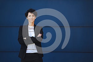 Portrait of confident mature female entrepreneur standing with arms crossed against blue wall