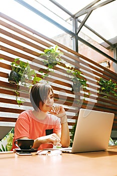 Portrait of confident mature professional woman in glasses, a coral T-shirt sitting on summer terrace in cafe, using laptop