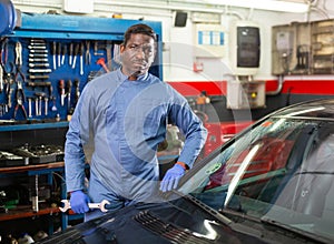 Portrait of confident mechanician posing near car at service