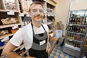 Portrait of confident mid adult salesman standing hands on hips in grocery store