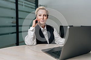 Portrait of confident middle-aged businesswoman, company executive, CEO sitting at desk with laptop, looking at camera