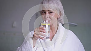 Portrait of confident middle aged grey-haired woman toasting drinking detox lemon water in slow motion gesturing thumb