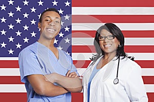 Portrait of confident mixed race male and female surgeons over American flag