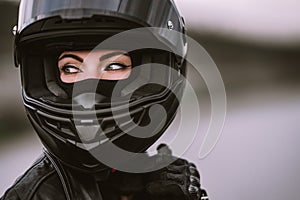 Portrait of confident motorcyclist woman in motorcycle helmet. Young driver biker looking away outdoors. Cafe racers