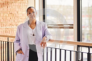 Portrait of confident multiracial LGBTQ mid adult woman leaning on railing in modern office space