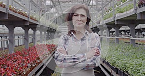 Portrait of confident positive woman posing in greenhouse. Mid-adult brunette employee agronomist crossing hands and