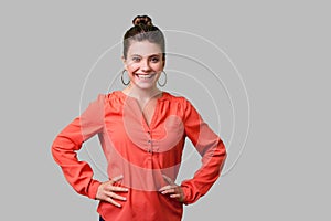 Portrait of confident positive young woman with bun hairstyle, big earrings and in red blouse. indoor studio shot isolated on gray