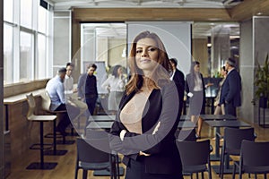 Portrait of confident and proud young woman against background of her office colleagues.