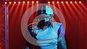 Portrait of confident quarterback agressive looking at camera. American football player in team uniform and helmet