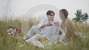 Portrait of confident relaxed man and woman toasting sitting on picnic talking in slow motion. Wide shot carefree