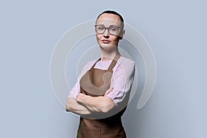 Portrait of confident serious 30s woman in apron on grey studio background