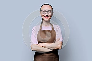 Portrait of confident smiling 30s woman in apron on grey studio background