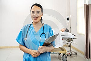 Portrait of confident smiling asian female doctor, nurse in standing smiling in a blue lab shirt holding patient documents in hand