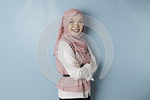 Portrait of a confident smiling Asian Muslim woman standing with arms folded and looking at the camera  over blue
