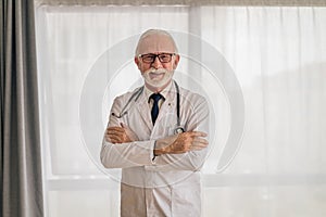 Portrait of confident smiling elderly doctor standing with arms crossed