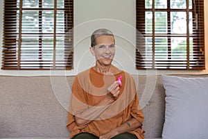Portrait of confident smiling elderly senior woman with pink ribbon at her home. Health care, support, prevention