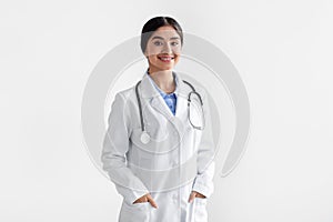 Portrait of confident smiling millennial indian female doctor in white coat with stethoscope