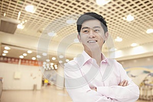 Portrait of confident smiling young businessman in button down shirt with arms crossed, indoors