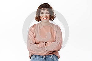 Portrait of confident smiling young woman, cross arms on chest, smiles and looks with determines and self-assured