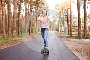 Portrait of confident sporty energetic young female listening to music, putting on headphones, having roller blades on legs,