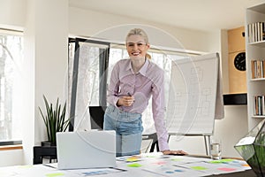 Portrait of confident successful businesswoman standing at table in office