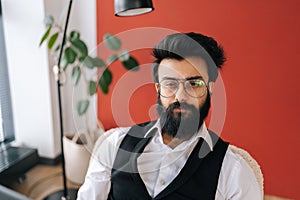 Portrait of confident successful Indian business man in elegant formalwear posing coworking office by window. Bearded