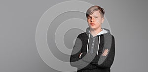 Portrait of confident teenage boy looking at the camera, posing over gray background with crossed hands, wearing in casual clothes