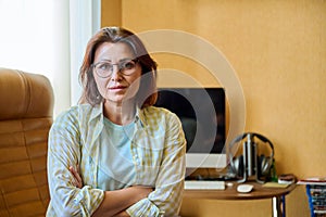 Portrait of confident woman looking at camera with crossed arms at home workplace