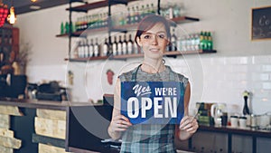Portrait of confident woman small business owner holding We Are Open sign standing in her coffee shop and smiling