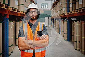 Portrait of confident worker wearing helmet and spectacles with orange vest uniform standing in aisle of heavy duty