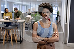 Portrait of confident young african american businesswoman standing with arms crossed at workplace