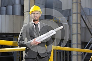 Portrait of confident young architect holding blueprints outside industry