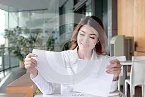 Portrait of confident young Asian business woman analyzing charts or paperwork in her hands in office