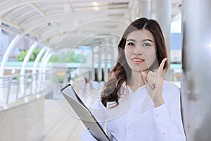 Portrait of confident young Asian business woman holding document folder and looking at camera at outside office
