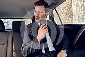 Portrait of confident young business man in full suit looking away seriosly with mobile phone in hand while sitting in the car