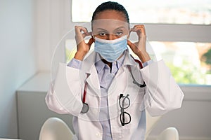 Portrait of confident young female doctor putting on mask