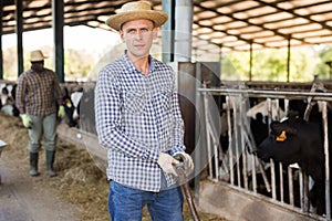 Portrait of a confident young male farmer standing in a cowshed with a shovel