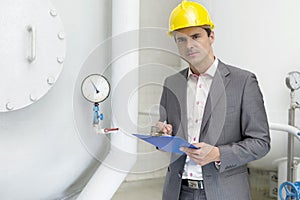 Portrait of confident young male inspector writing on clipboard in industry