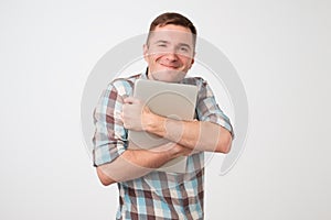 Portrait of confident young man holding laptop standing against white wall.