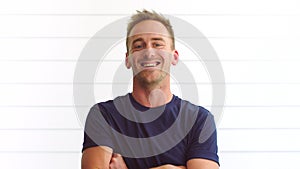 Portrait of a confident young man smiling and laughing against a white background while standing with his arms crossed