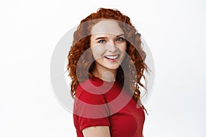 Portrait of confident young pretty woman with curly red hair, natural pale skin and light make-up, showing her candid