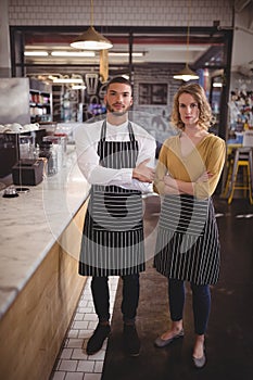 Portrait of confident young wait staff standing with arms crossed by counter