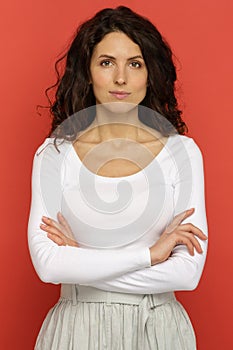 Portrait of confident young woman with light smile and crossed hands standing over red studio wall