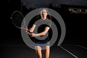 portrait of confident young woman playing tennis with tennis racket. Dark background