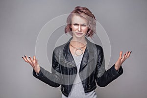 Portrait of confused beautiful girl with short hairstyle and makeup in casual black leather jacket standing with raised arms and