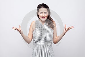 Portrait of confused beautiful young brunette woman with makeup and striped dress standing and looking at camera with angry face